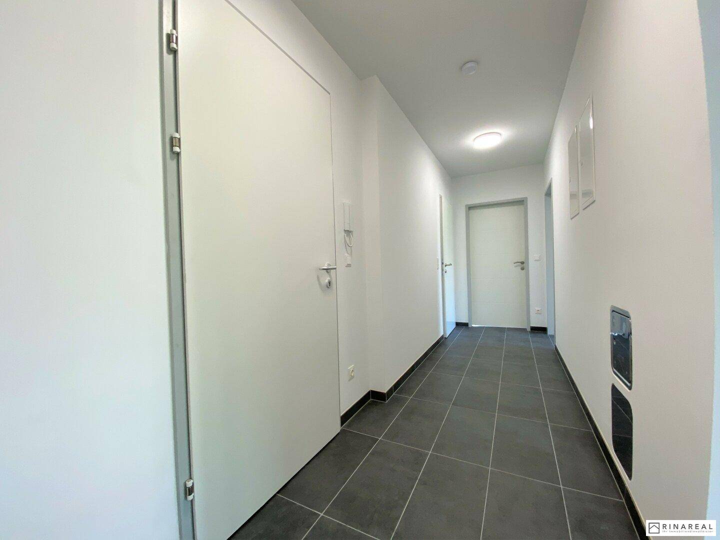 Heller Flur mit dunklen Fliesen und Zugang zu den verschiedenen Räumen der Wohnung.