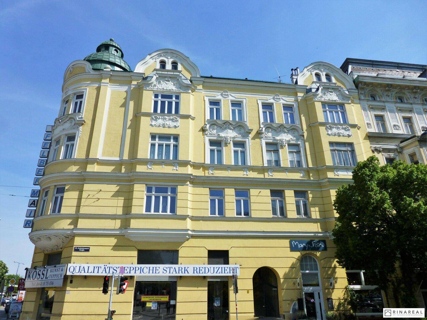 Gelbes historisches Gebäude mit reich verzierten Fassadendetails und Geschäften im Erdgeschoss unter blauem Himmel.