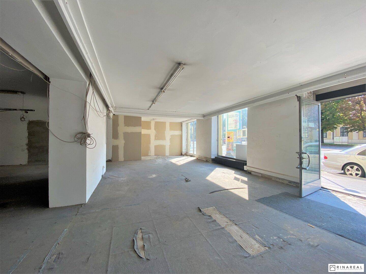 Heller Gewerberaum mit großen Fenstern, Betonboden und sichtbaren Trockenbauwänden, bereit für den Ausbau.
