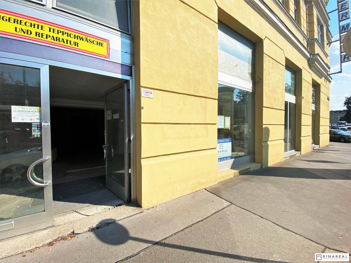 Gelbe Gebäudefassade mit großen Schaufenstern und Eingangsbereich direkt an der belebten Straße.