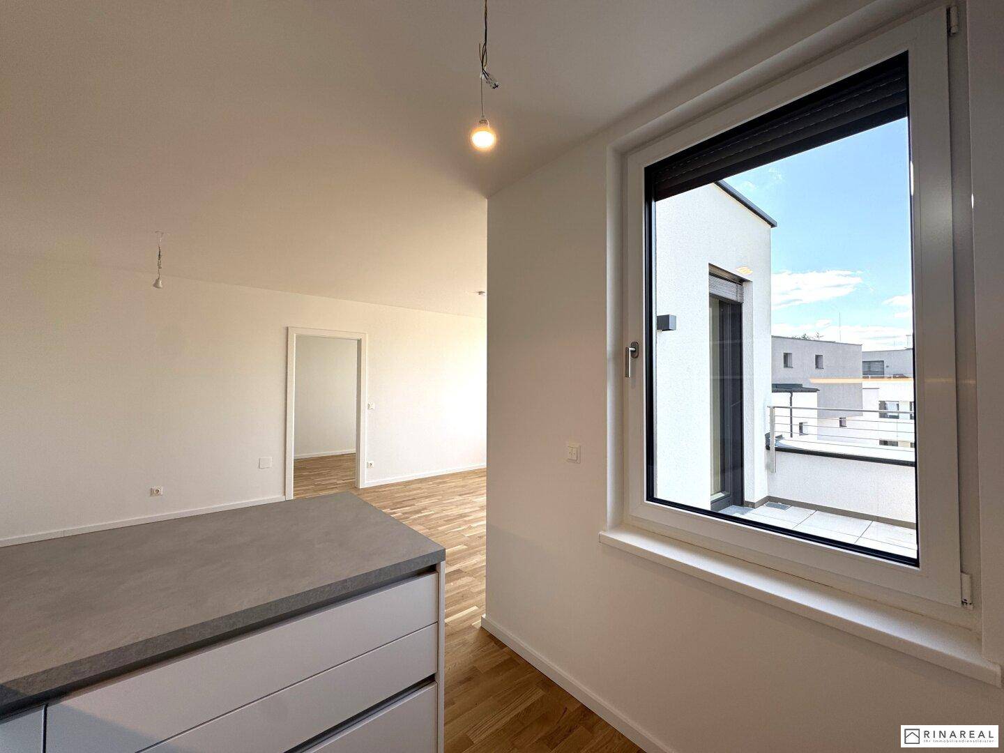 Küchenbereich mit Fenster und Blick auf die umliegenden Gebäude und den Außenbereich, hell und praktisch.