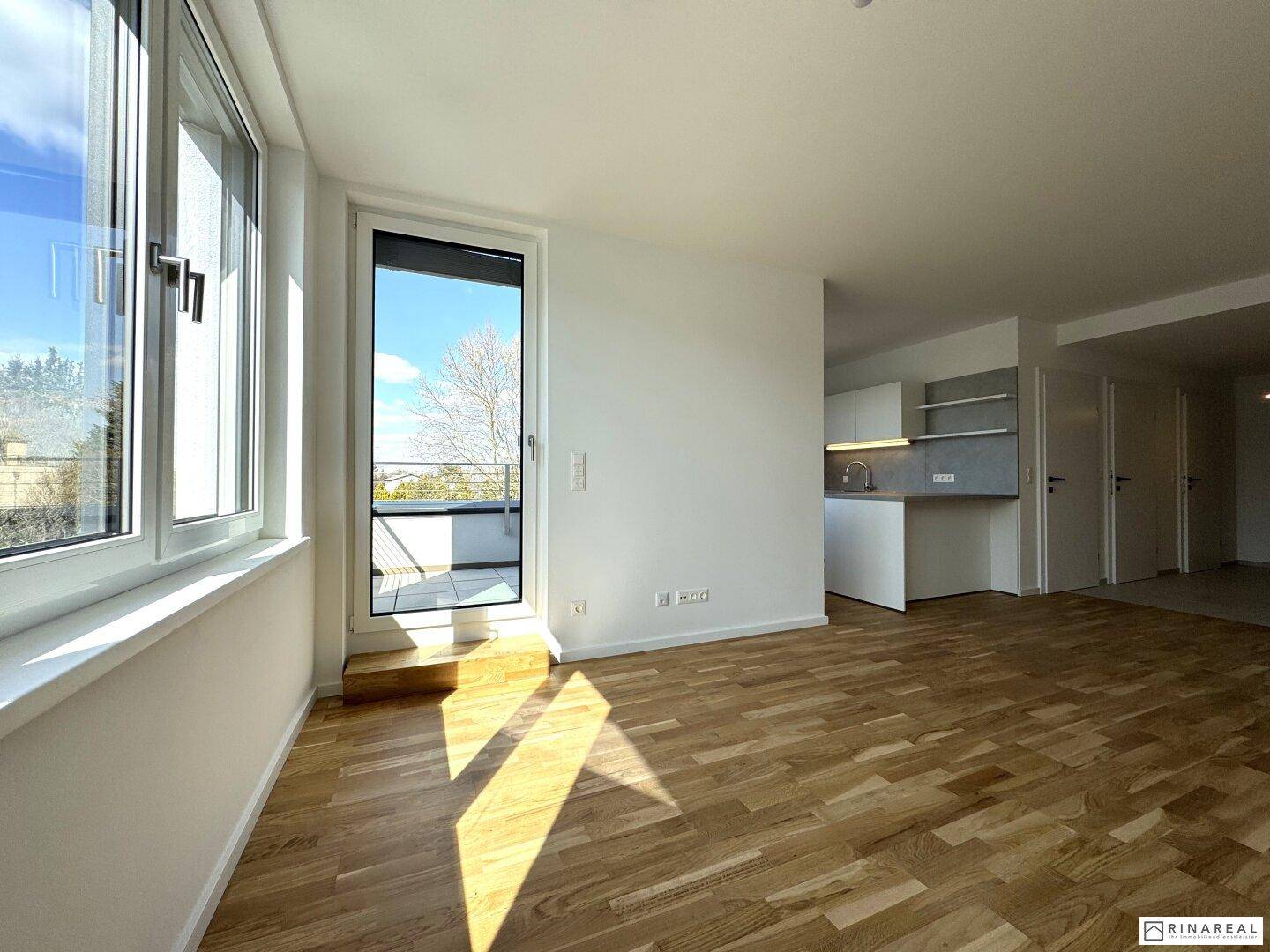 Heller Wohnbereich mit Holzboden, großen Fenstern und direktem Zugang zum Außenbereich, modern gestaltet.