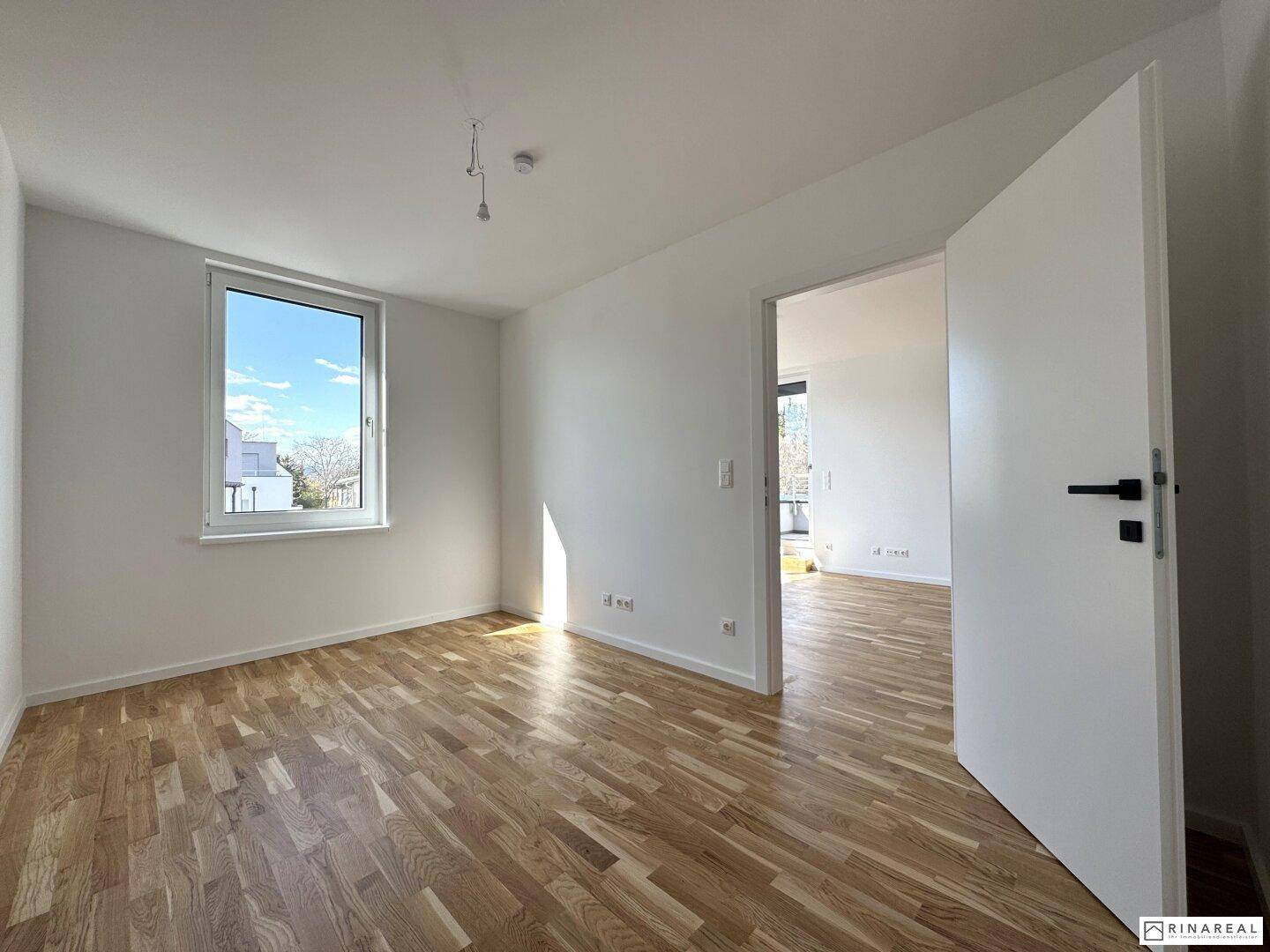 Helles Schlafzimmer mit Parkettboden, weiß gestrichenen Wänden und einem großen Fenster, ruhig und gemütlich.