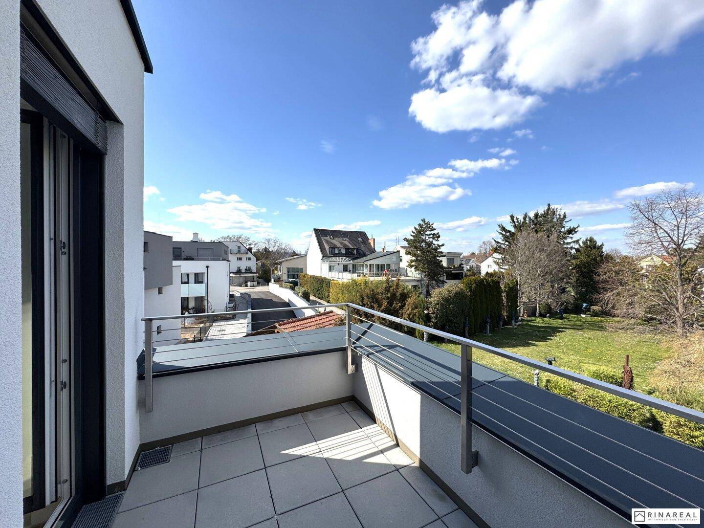 Geräumiger Balkon mit Weitblick über Gärten und die Nachbarschaft an einem sonnigen Tag mit blauem Himmel.