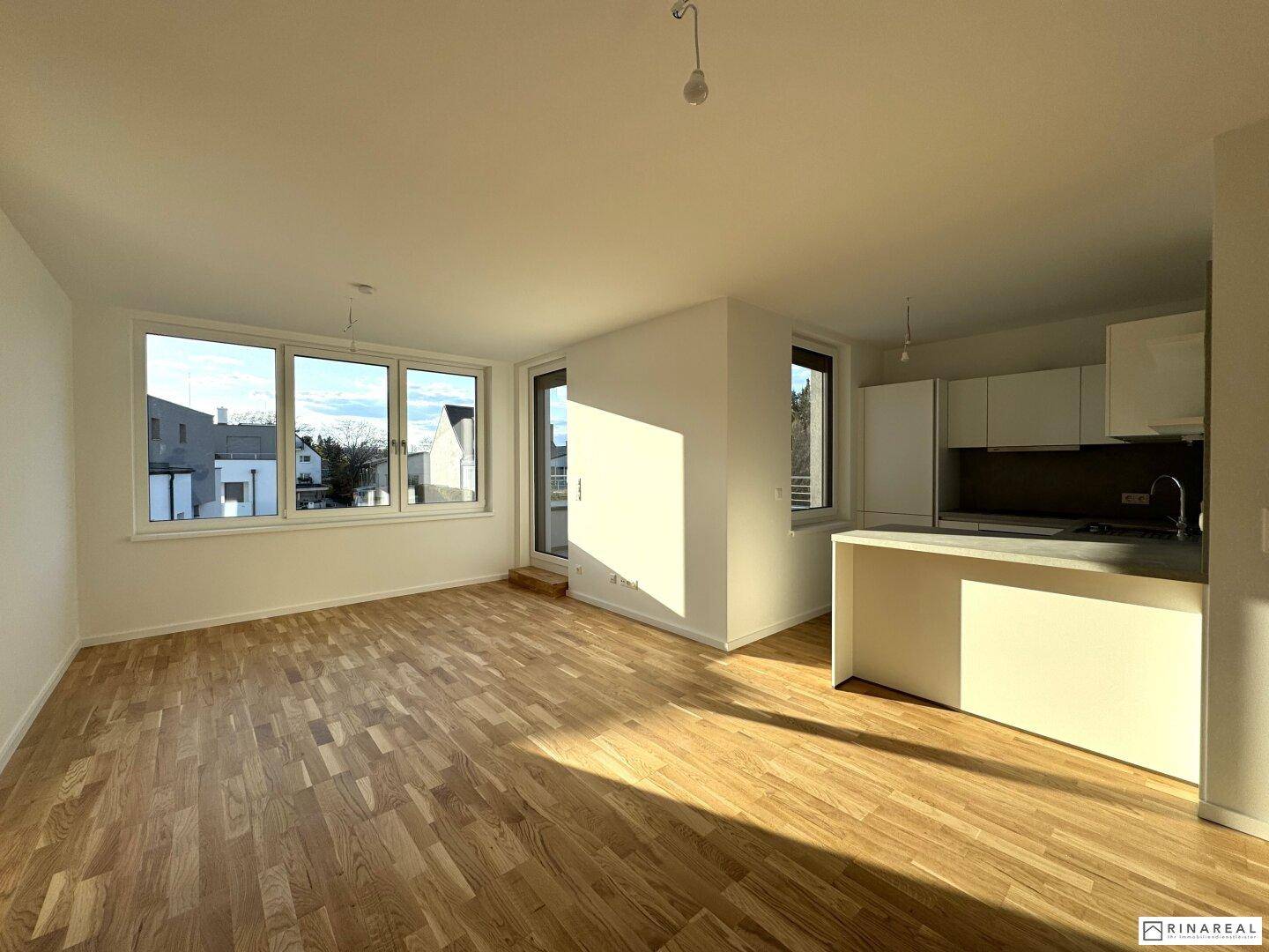 Offener Wohnbereich mit moderner Küche, Parkettboden und Zugang zu einem Balkon, lichtdurchflutet.