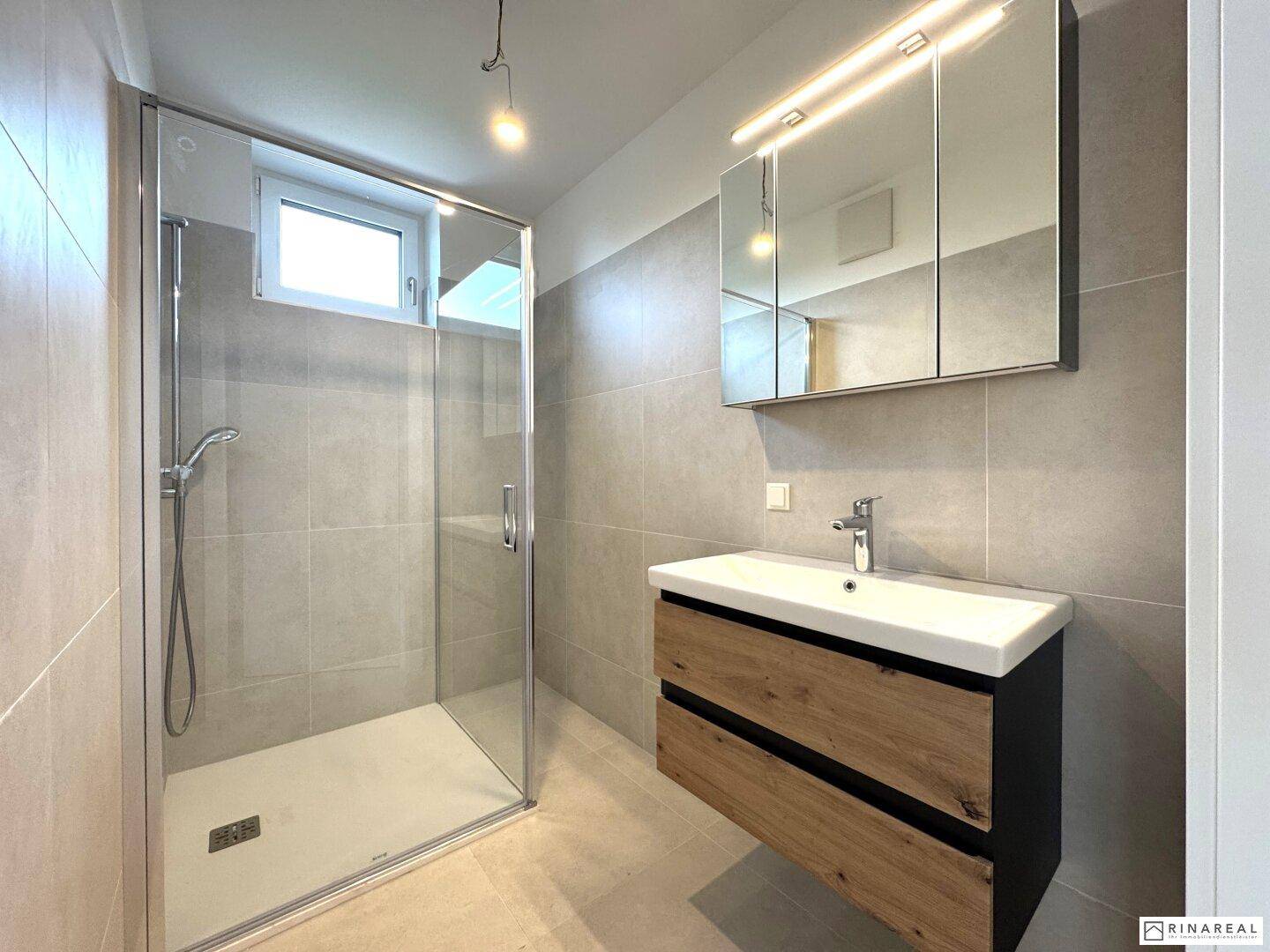 Modernes Badezimmer mit begehbarer Dusche, Holzwaschtisch und Spiegelschrank, hell gefliest und funktional.