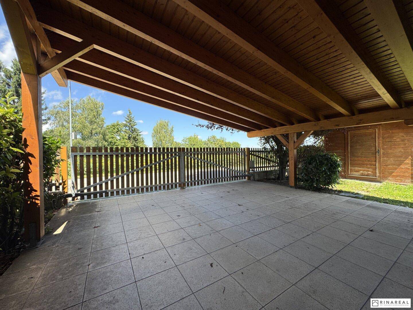 Überdachter Carport mit gefliestem Boden und Holzbalken, bietet Schutz für Fahrzeuge.