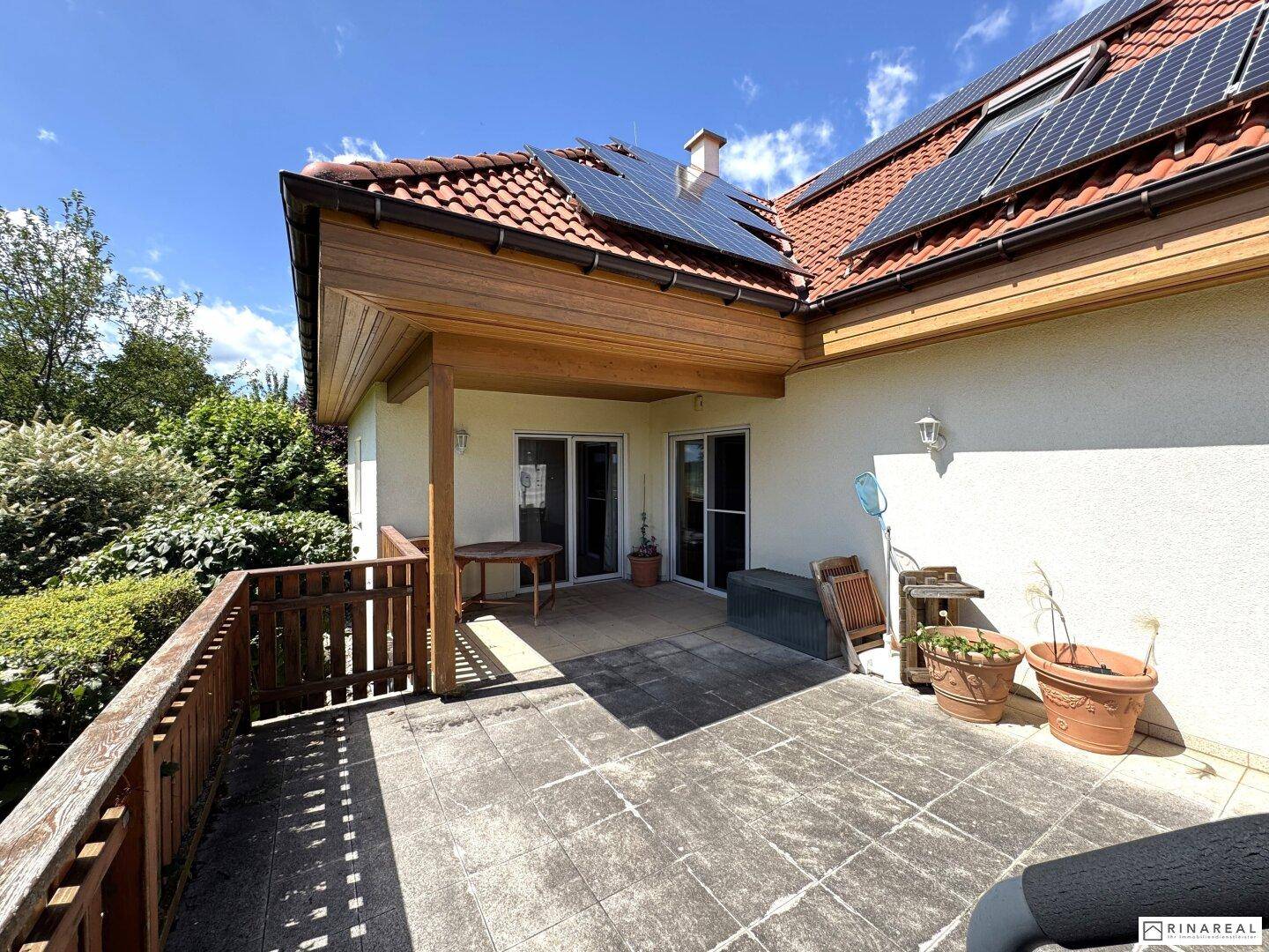 Hintere Terrasse mit Zugang zum Haus, umgeben von Grün und mit Solaranlage auf dem Dach.