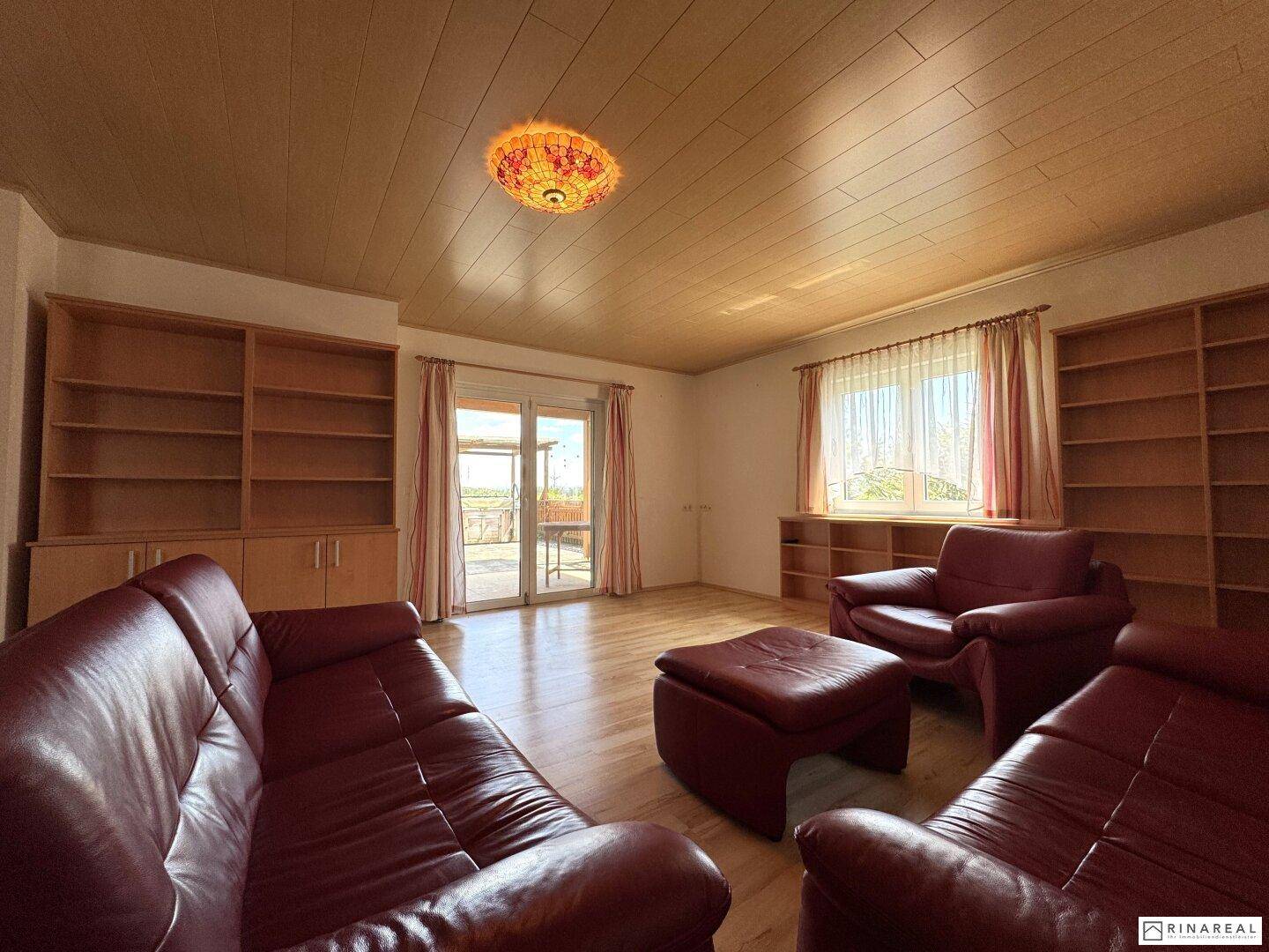 Gemütliches Wohnzimmer mit Holzboden, roten Ledersofas und Zugang zur Terrasse.