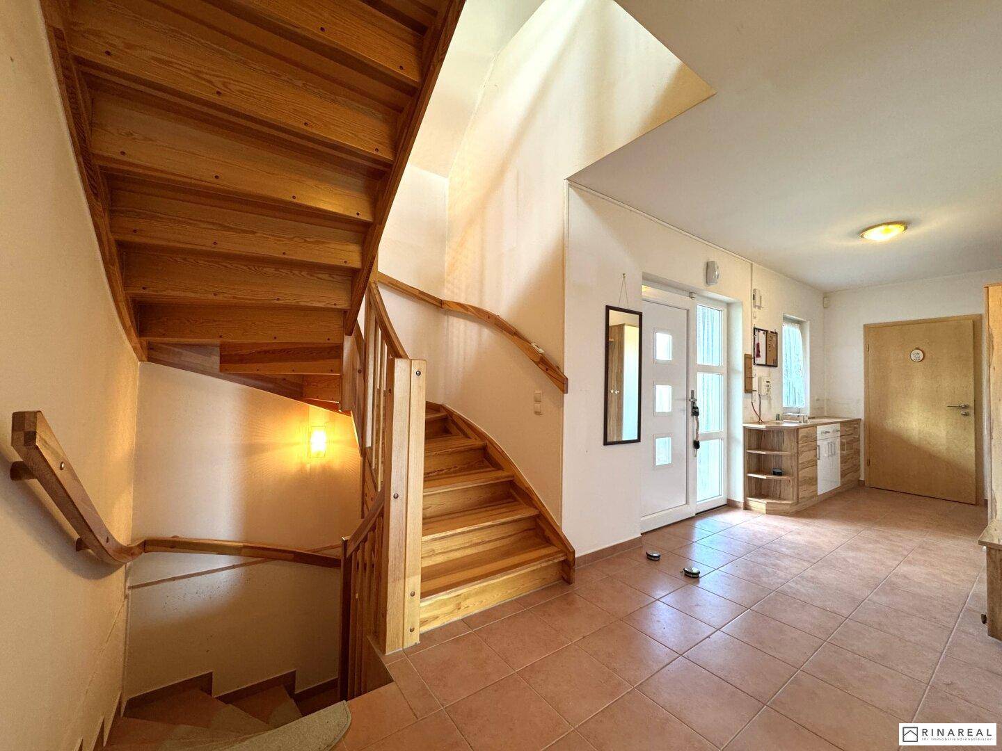 Geräumiger Eingangsbereich mit Holztreppe, gefliestem Boden und Zugang zu weiteren Räumen.