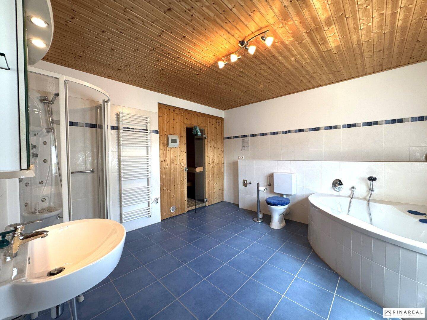 Großes Badezimmer mit blauen Fliesen, Eckbadewanne, Dusche, Sauna und Holzdecke.