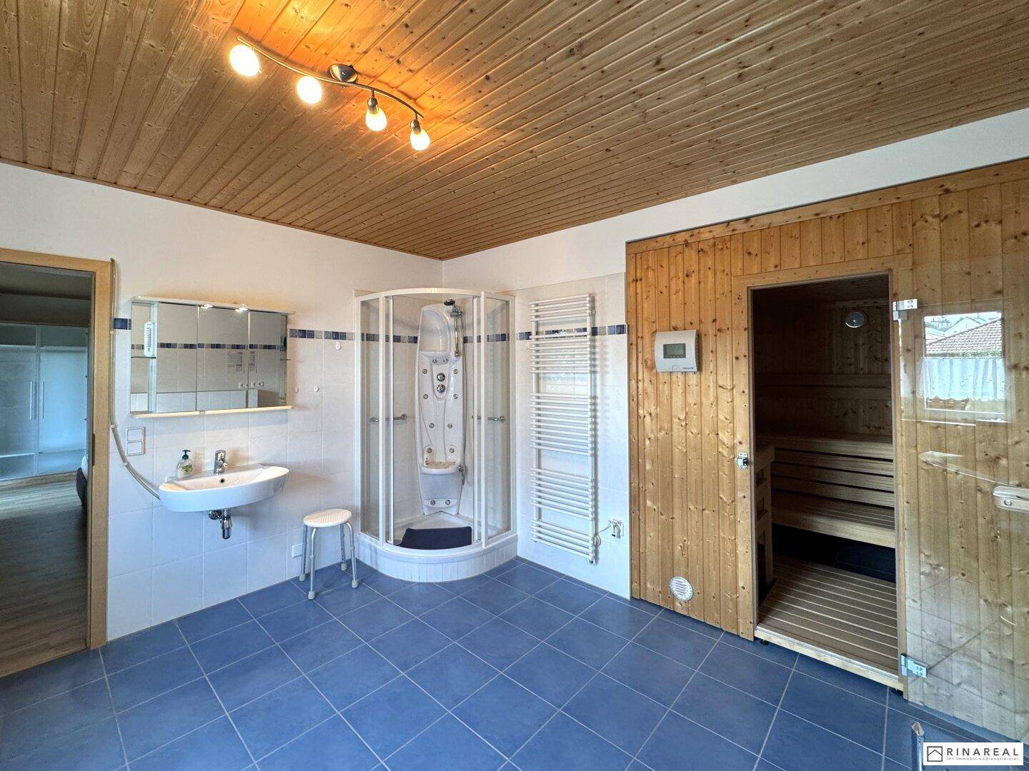 Geräumiges Badezimmer mit Sauna, Duschkabine, Waschbecken und blauen Bodenfliesen.