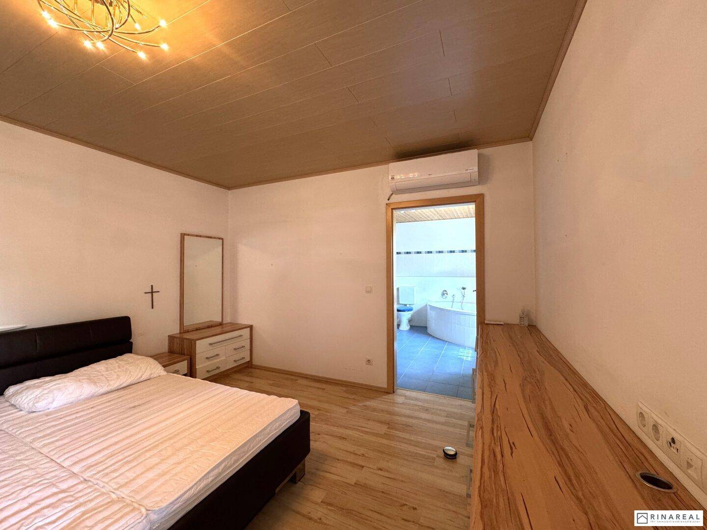 Schlafzimmer mit Holzboden, Klimaanlage und direktem Zugang zu einem Badezimmer.