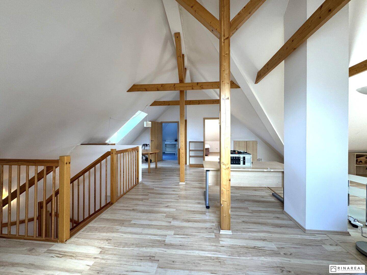 Heller, ausgebauter Dachboden mit Holzbalken, Laminatboden und Dachfenstern.