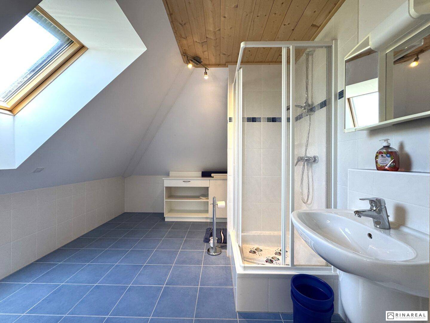 Badezimmer im Dachgeschoss mit blauen Fliesen, Duschkabine, Waschbecken und Dachfenster.