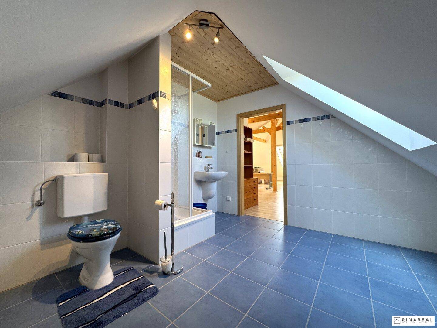 Helles Dachgeschoss-Badezimmer mit blauen Fliesen, Toilette, Dusche und Dachfenster.