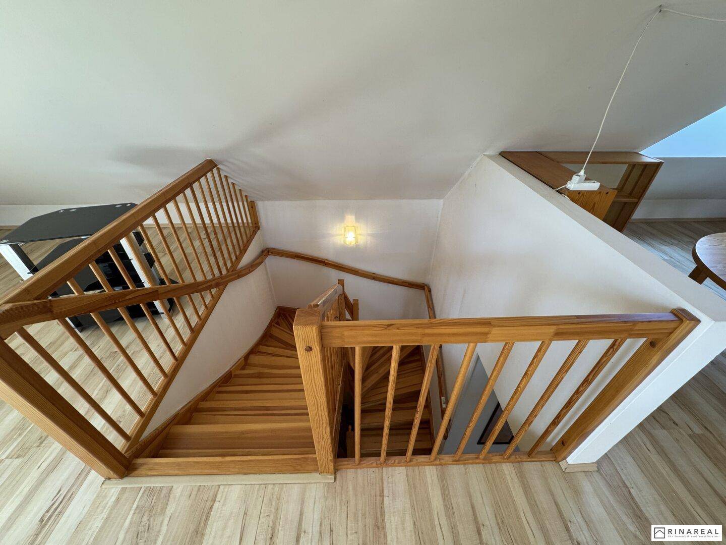Holztreppe führt in den ausgebauten Dachbodenbereich mit schrägen Wänden.