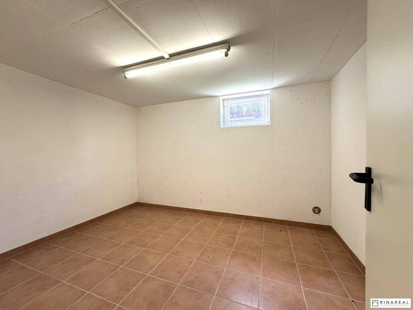 Heller Kellerraum mit gefliestem Boden und kleinem Fenster, ideal als Abstell- oder Hobbyraum.