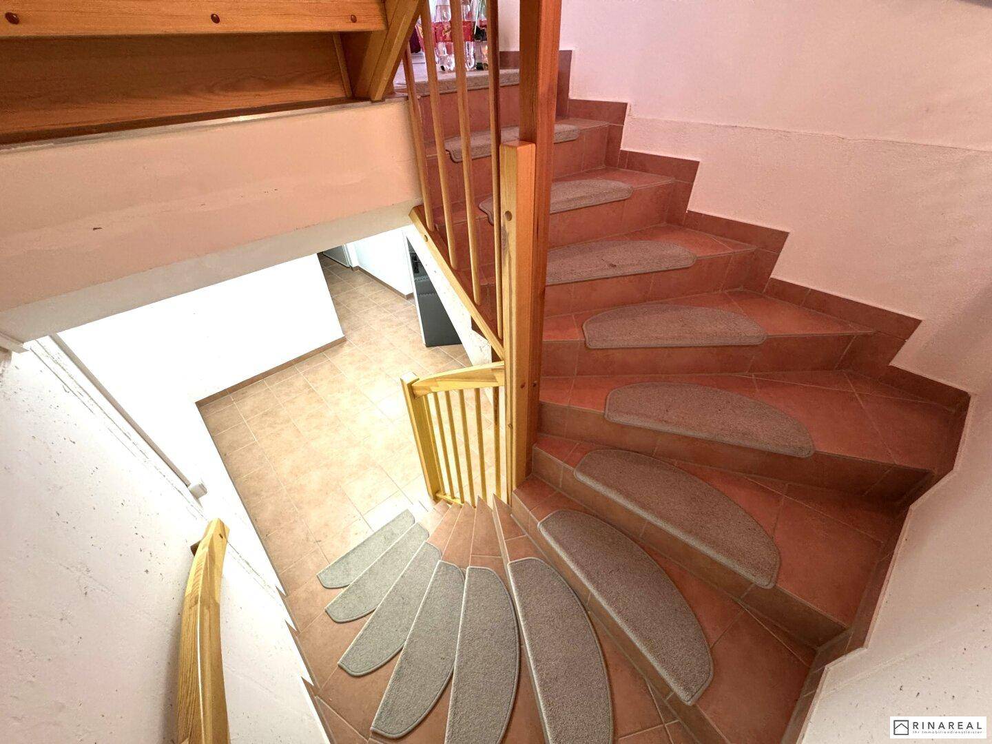 Wendeltreppe mit gefliesten Stufen und Teppichauflagen führt in das Untergeschoss.