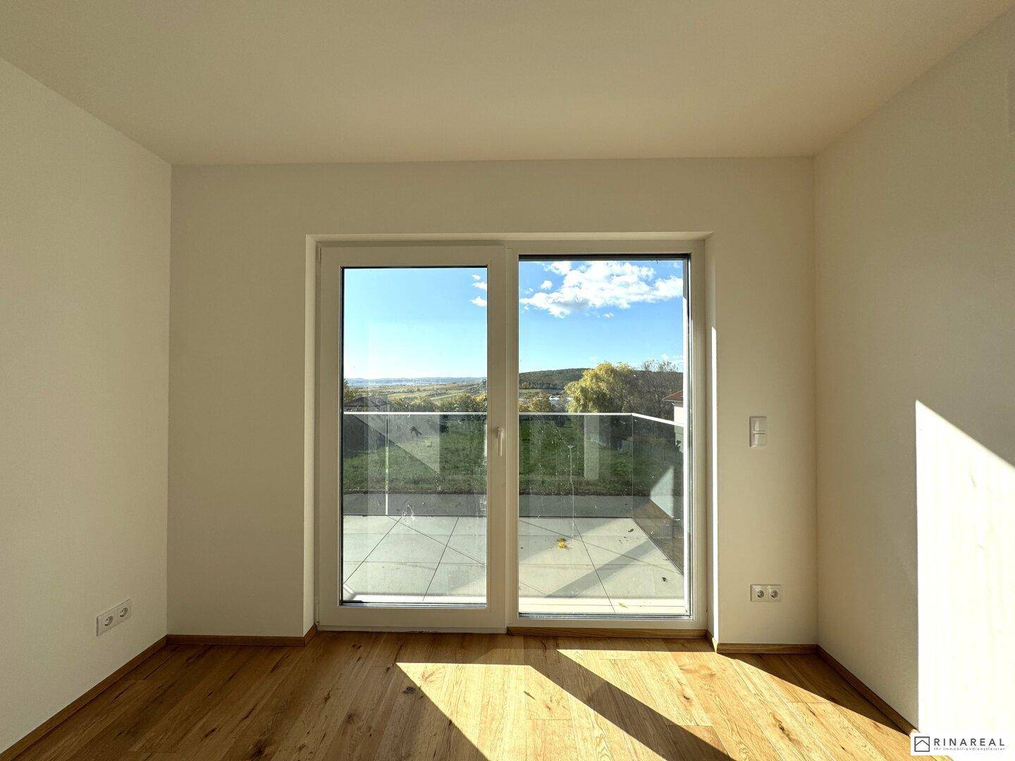 Helles Zimmer mit Holzboden und Schiebetür, die Zugang zu einem Balkon bietet.