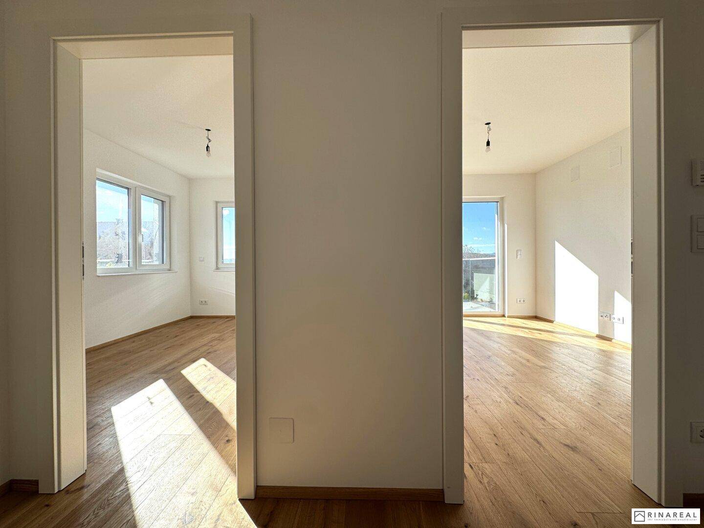 Flurbereich mit zwei Türen, die zu hellen Zimmern mit Holzboden und viel Tageslicht führen.