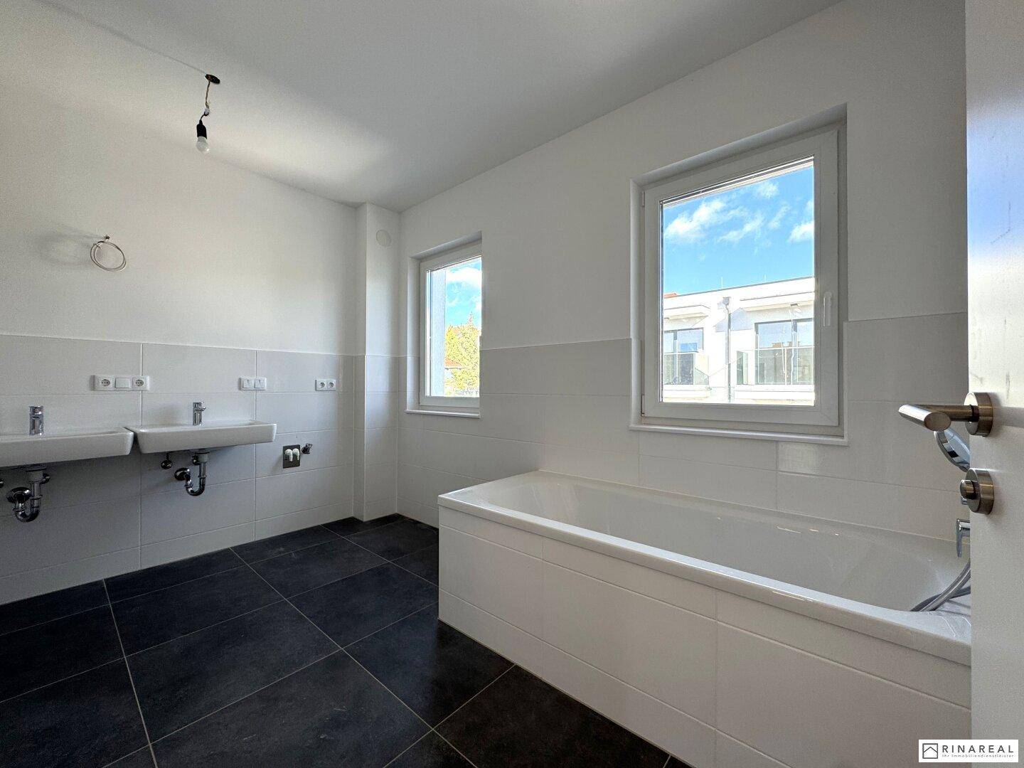 Modernes Badezimmer mit Badewanne, Doppelwaschbecken und dunklen Fliesen.