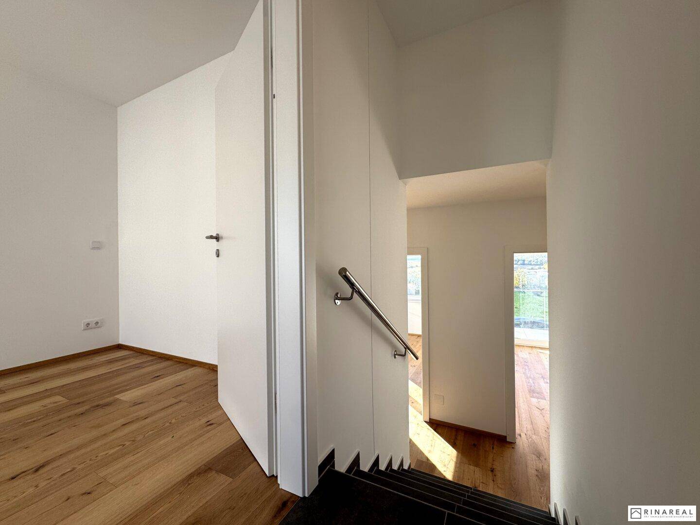 Heller Treppenbereich mit Holzboden im oberen Geschoss und weiß gestrichenen Wänden.