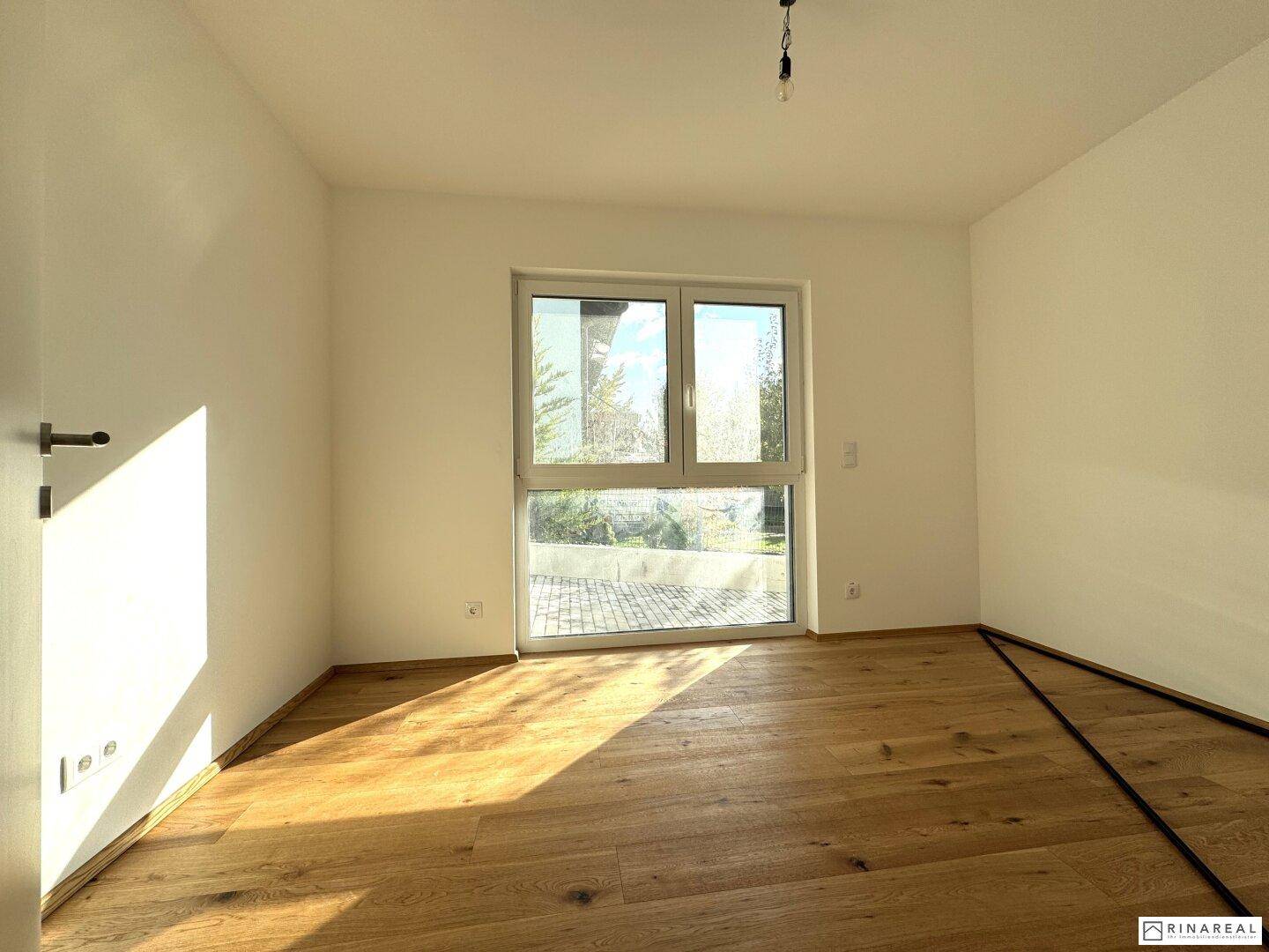 Geräumiges Schlafzimmer mit Holzboden und großem Fenster mit Zugang zum Außenbereich.