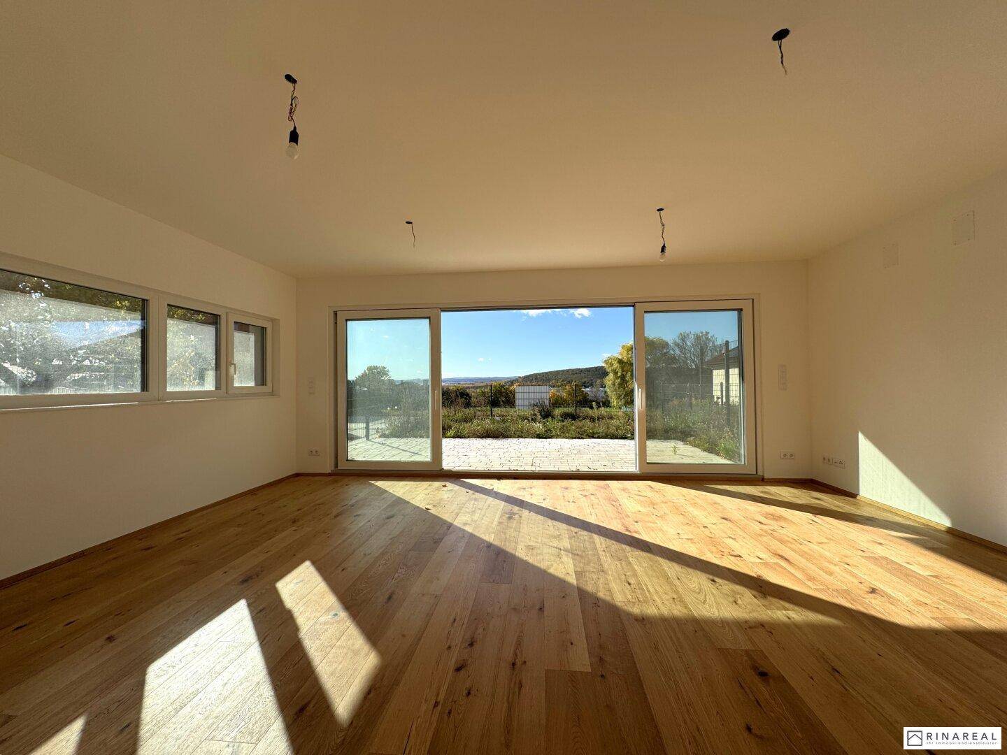 Lichtdurchfluteter Wohnraum mit Holzboden und weitem Blick in die Landschaft.