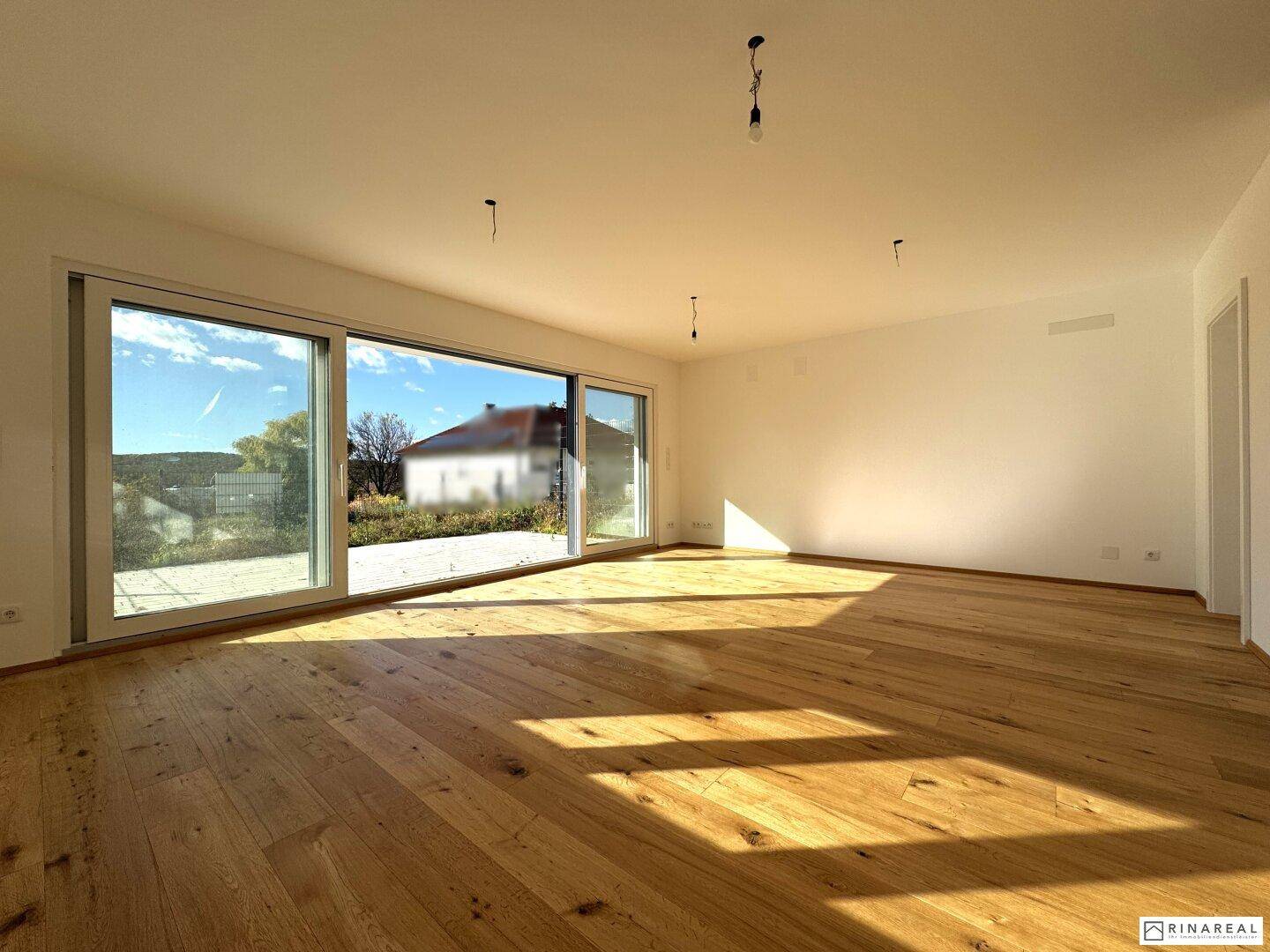 Lichtdurchfluteter Wohnraum mit Holzboden und weitem Blick ins Grüne durch große Fenster.
