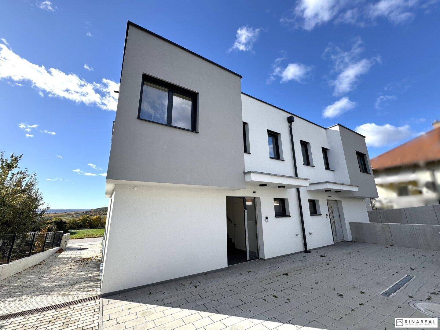 Moderne Reihenhäuser mit weißer und grauer Fassade und gepflasterter Zufahrt.