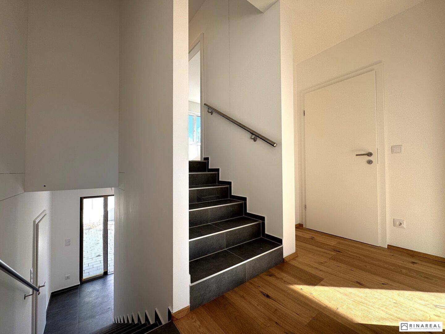 Moderne Treppe mit dunklen Fliesen und Edelstahlgeländer, die die Wohnebenen verbindet.