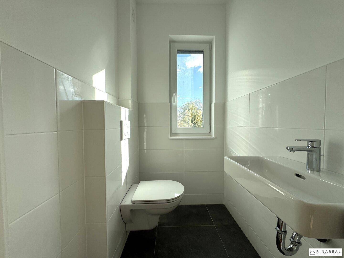 Modernes Gäste-WC mit wandhängendem WC, Waschbecken und schmalem Fenster.