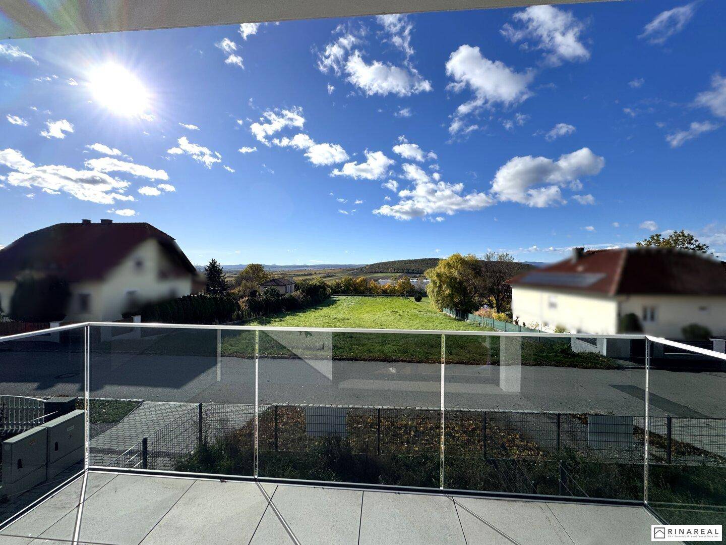 Sonniger Balkon mit Glasgeländer und weitem Blick über die grüne Landschaft.