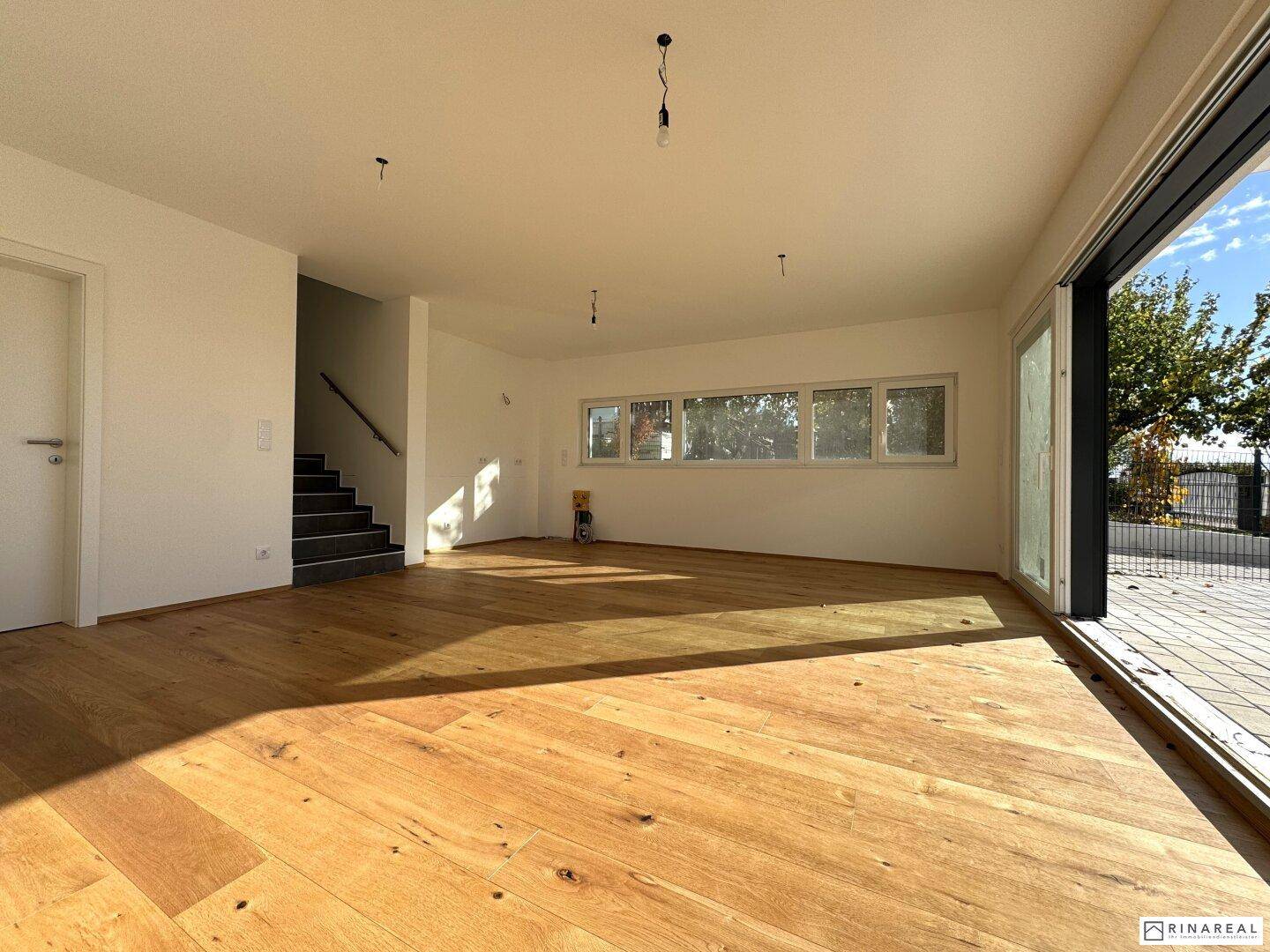 Geräumiger Wohnbereich mit Holzboden und Zugang zur modernen Treppe ins Obergeschoss.