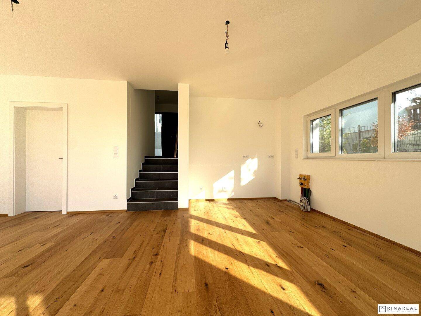 Heller Wohnraum mit Holzboden und Blick auf die moderne Treppe mit dunklen Stufen.