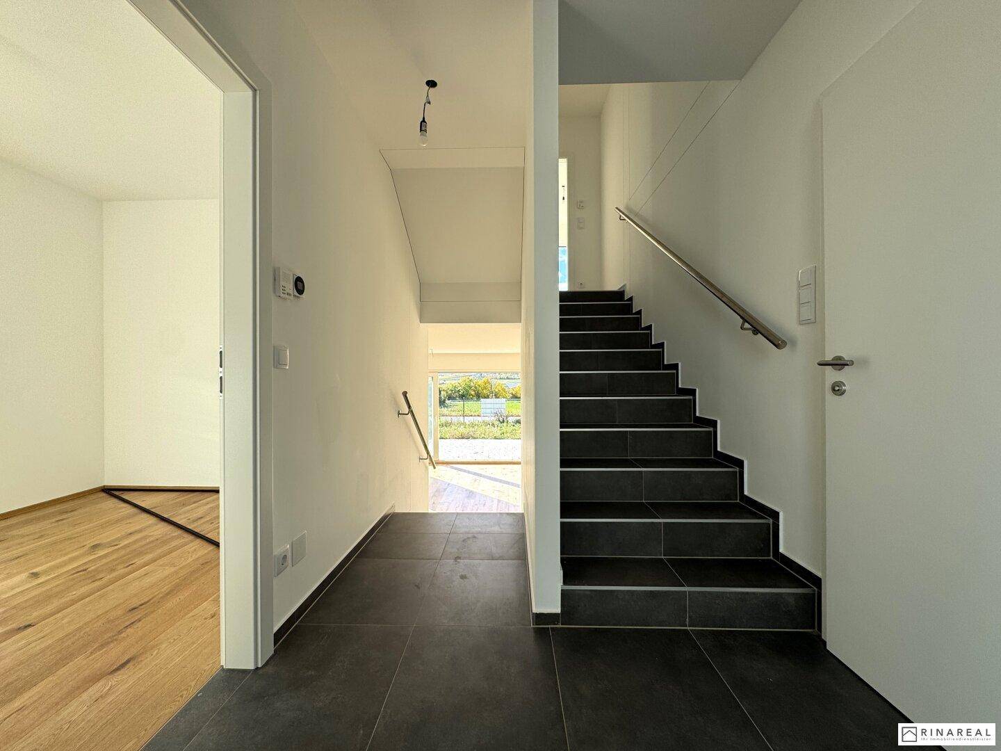 Heller Flur mit dunklen Fliesen und Treppe, die zu den oberen Etagen führt.