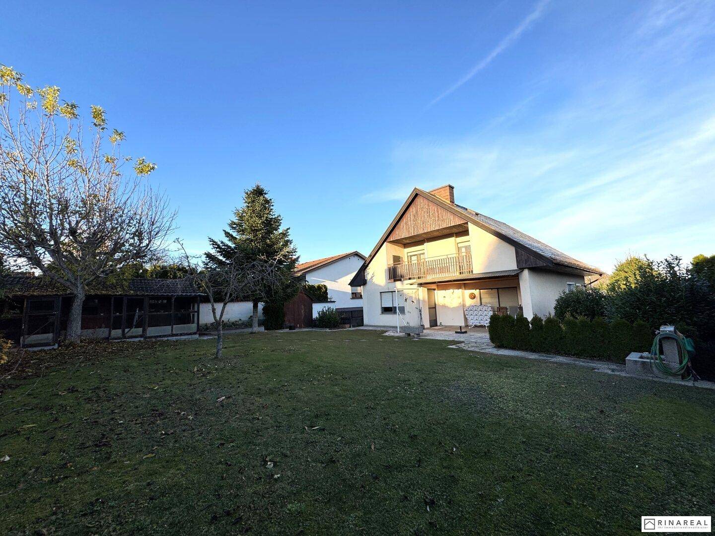 Weitläufiger Gartenbereich hinter dem Haus mit Rasenfläche und altem Baumbestand.