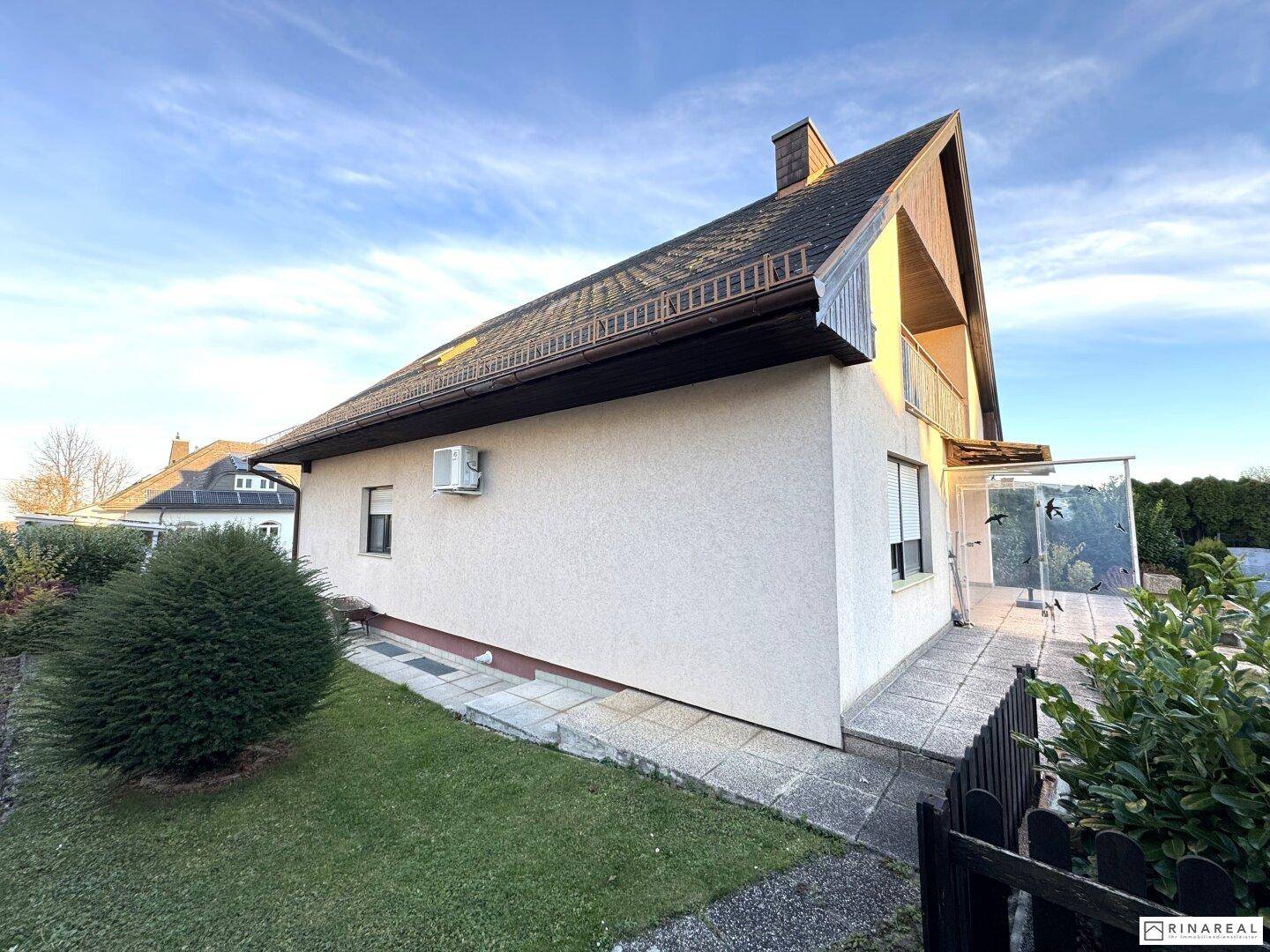 Seitenansicht des Hauses mit kleiner Terrasse und sichtbarer Klimaanlage an der Fassade.