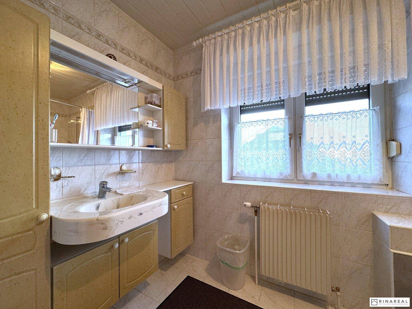 Badezimmer mit Fenster, Fliesenwänden und einem einzelnen Waschbecken.