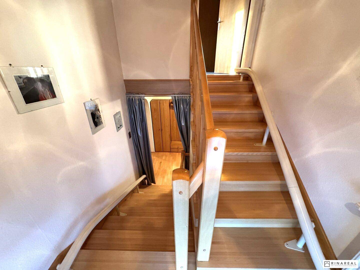 Holztreppe führt in das Obergeschoss, mit Handlauf und weiß gestrichenen Wänden.