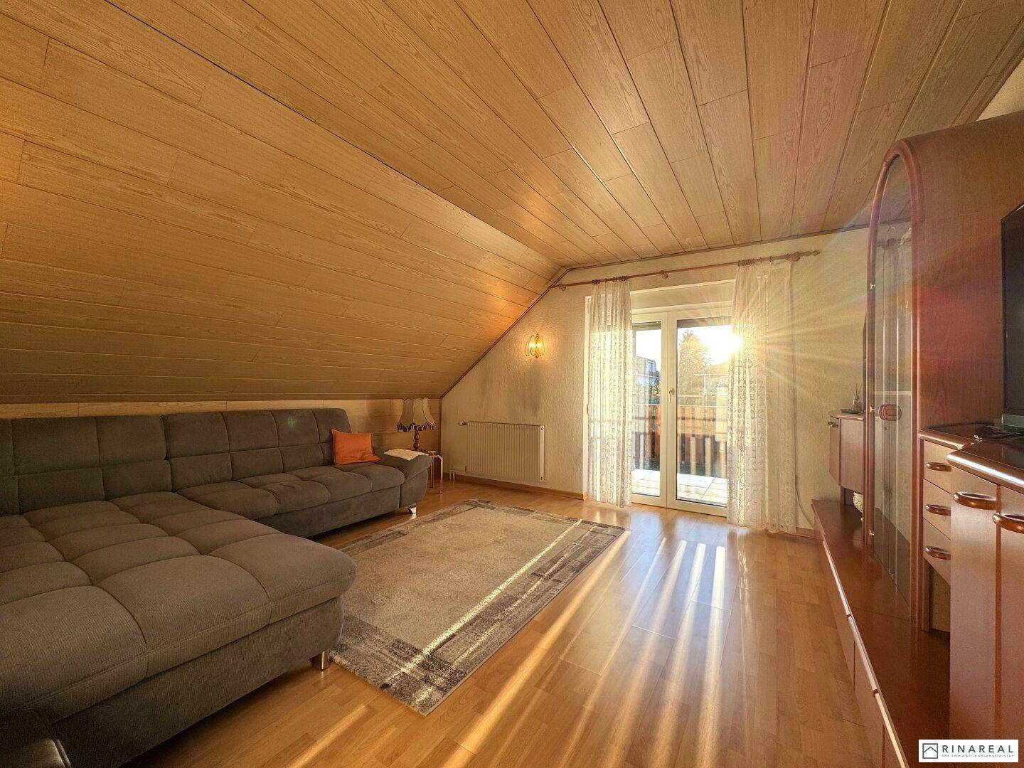 Gemütliches Wohnzimmer im Dachgeschoss mit Holzdachschrägen und Balkonzugang.