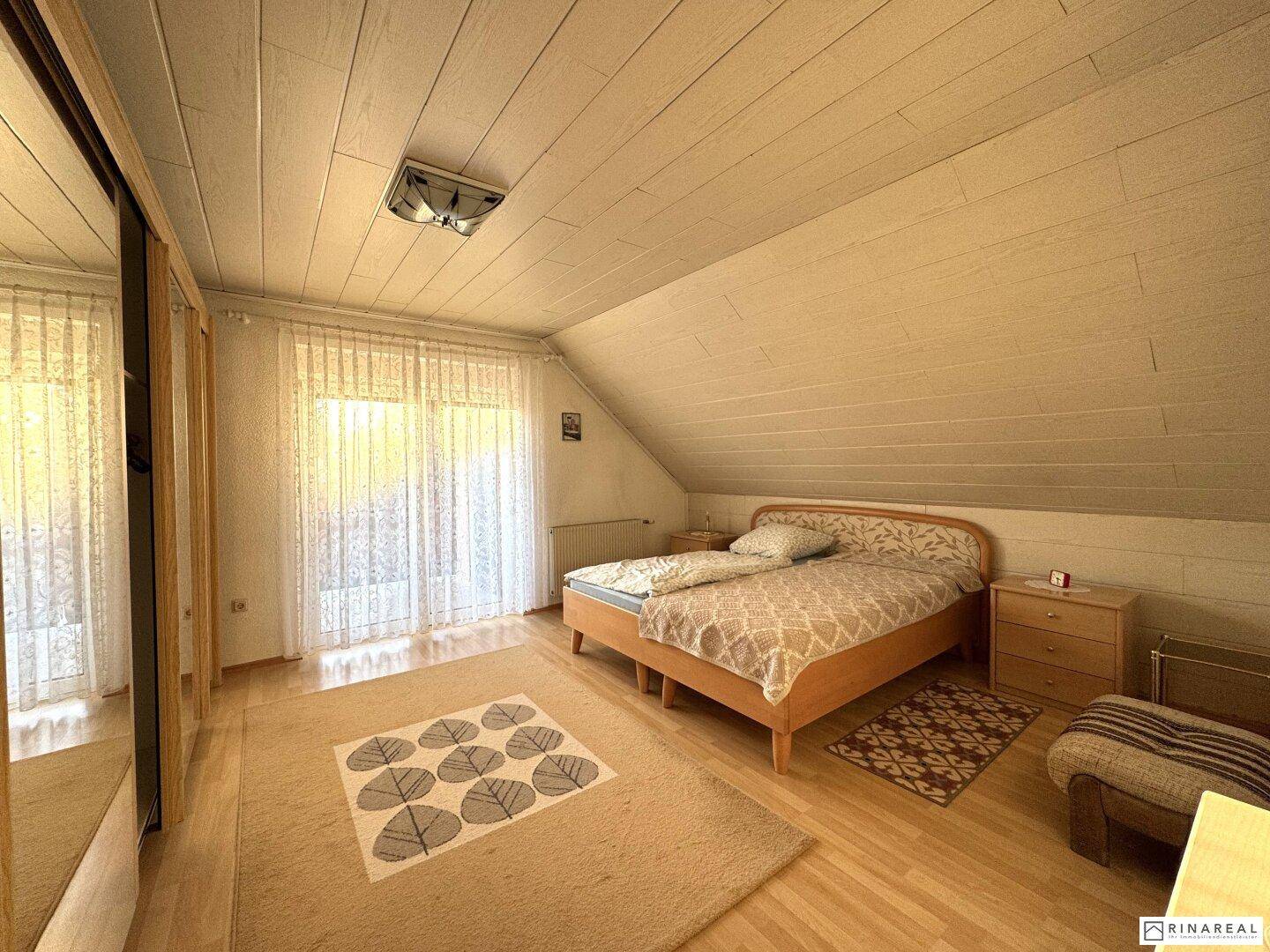 Helles Schlafzimmer im Dachgeschoss mit Holzdachschrägen und Parkettboden.