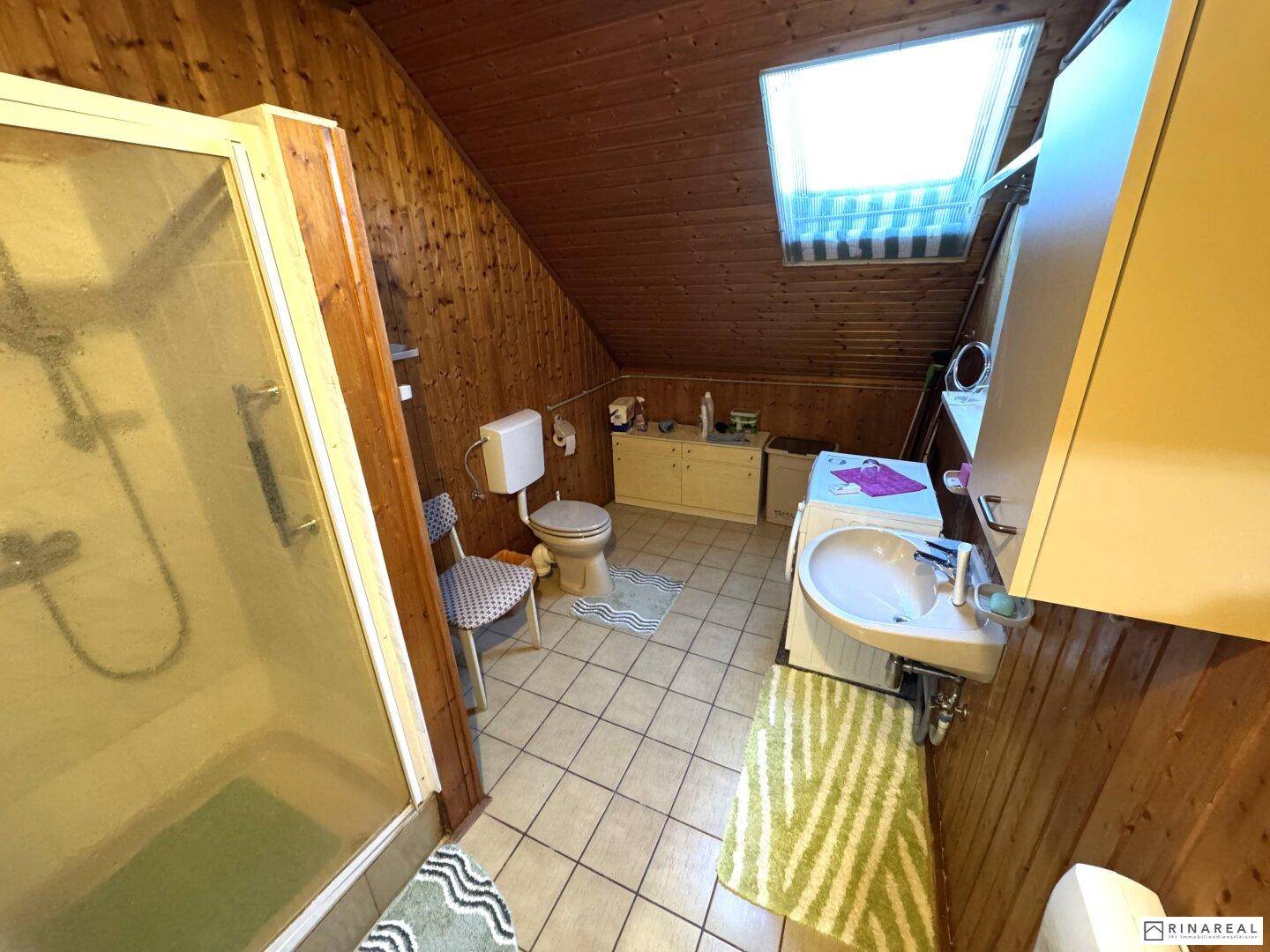 Badezimmer im Dachgeschoss mit Holzvertäfelung, Dusche und Dachfenster.