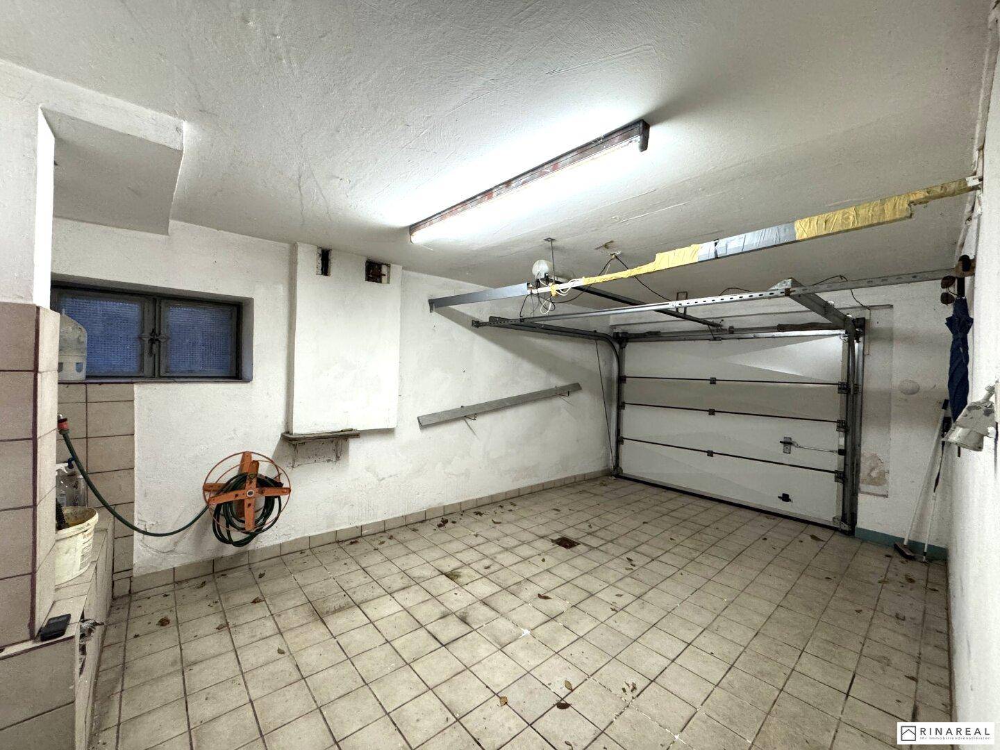 Geräumige Garage im Kellergeschoss mit Fliesenboden und Garagentor.