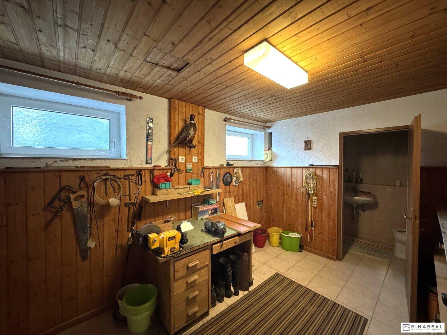 Werkstatt im Keller mit Holzvertäfelung, Werkbank und Fenstern.