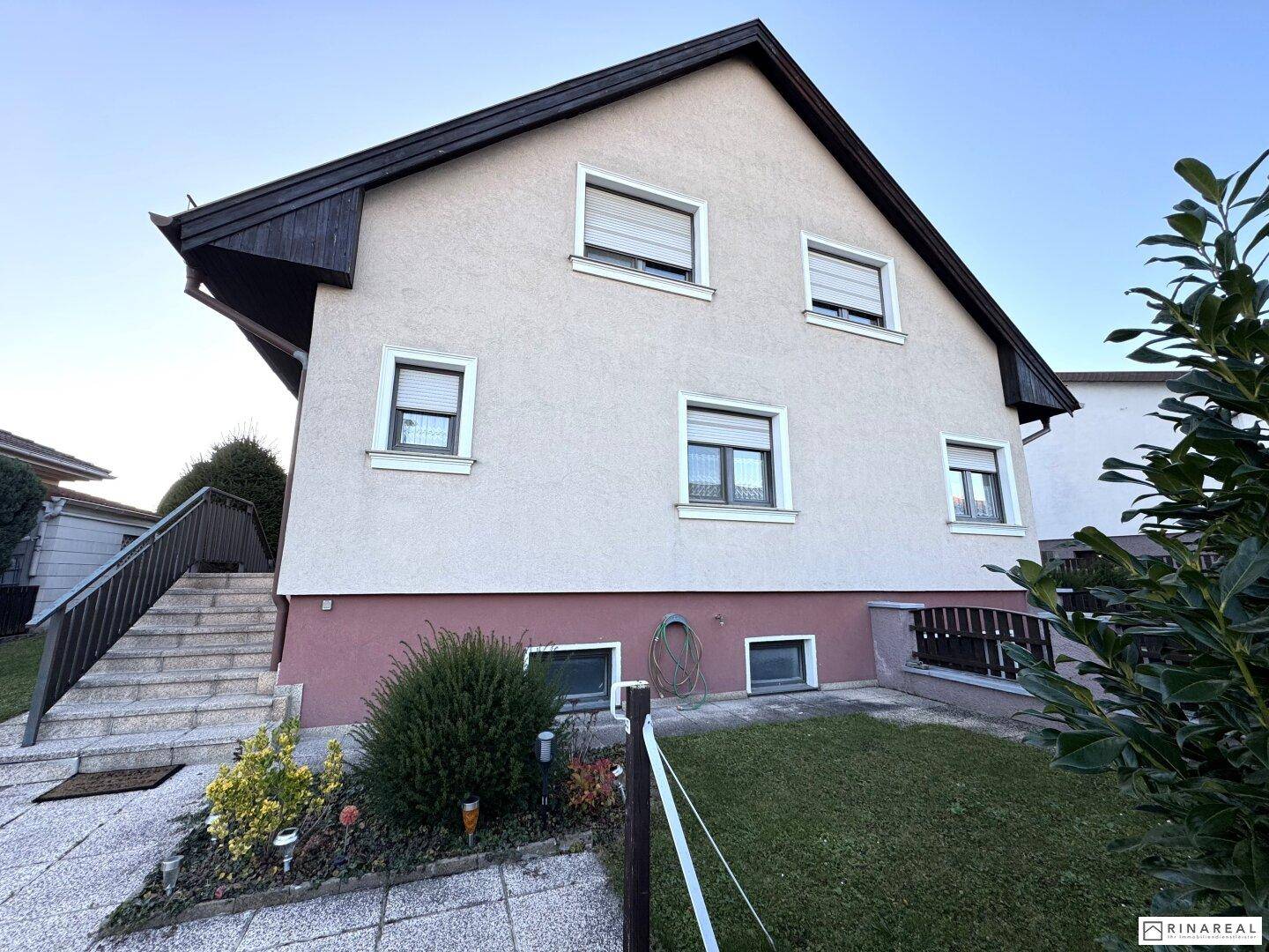 Vorderansicht des Hauses mit Fenstern und Rollläden, umgeben von Grünflächen.