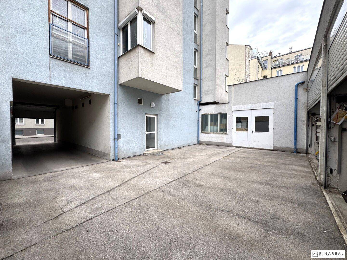 Betonierter Innenhof zwischen Gebäuden mit Zugang zu weiteren Bereichen und Parkmöglichkeiten.