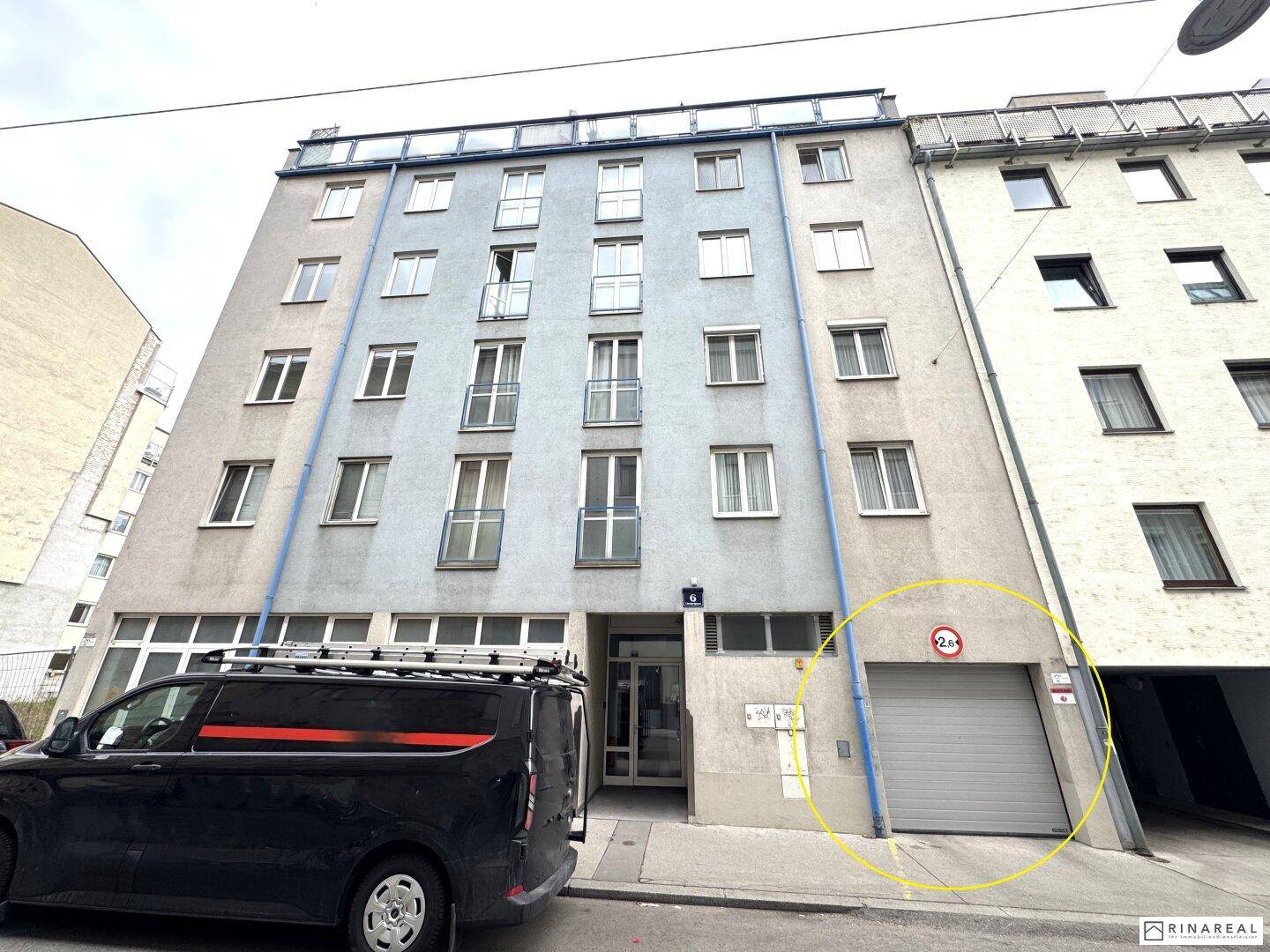 Fassade eines Mehrfamilienhauses mit Balkonen und der Zufahrt zur Tiefgarage von der Straße aus.