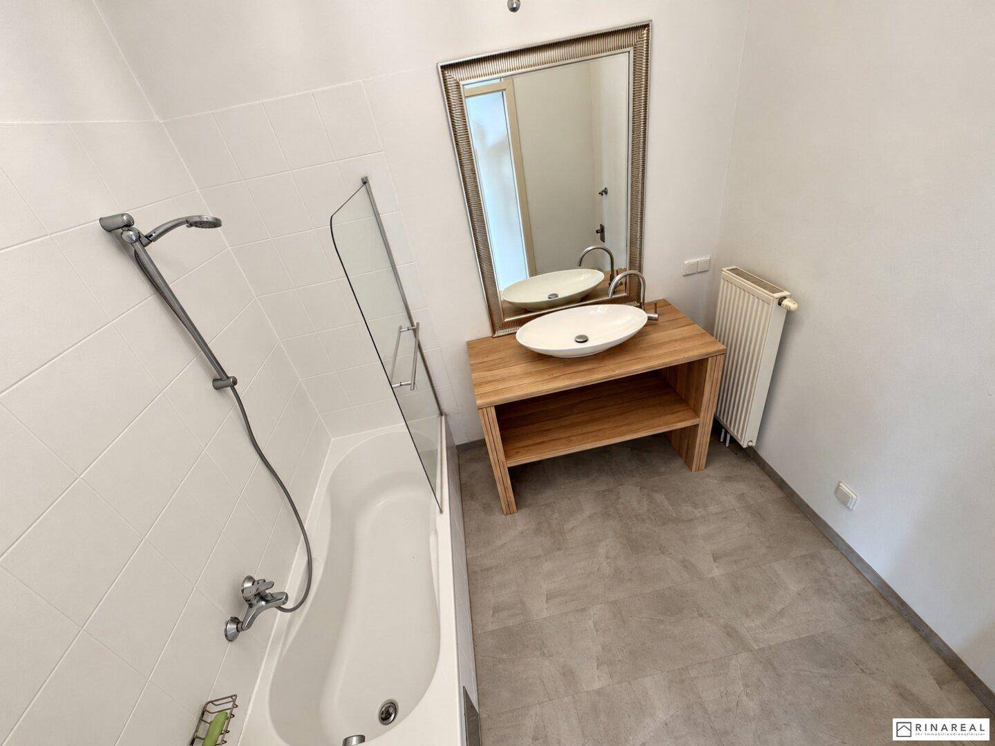 Helles Badezimmer mit Badewanne, modernem Waschbecken auf Holzunterschrank und großem Spiegel.